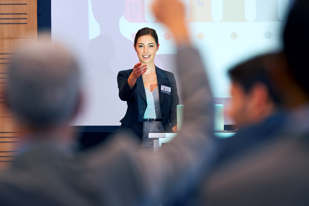 Mulher, durante uma apresentação, apontando para uma pessoa que levantou a mão para fazer uma pergunta