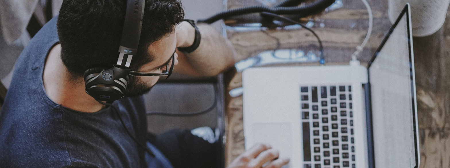 homem branco com fone de ouvido usando o computador para navegar por banco de imagens gratuito