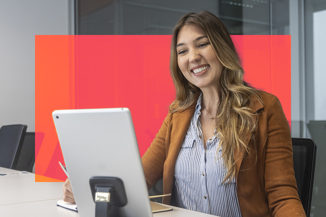 Mulher sorrindo e olhando para o computador, via comunicação assíncrona