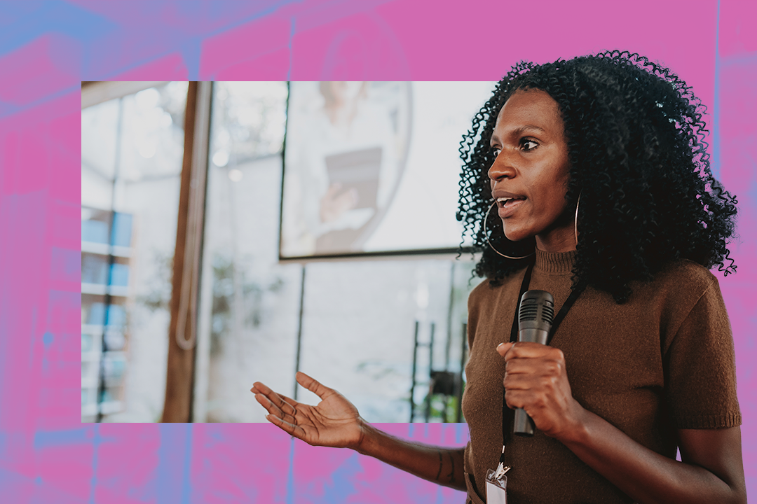 Mulher negra é mestre de cerimônias em um evento, segurando um microfone e interagindo com a audiência em um ambiente de conferência moderno.