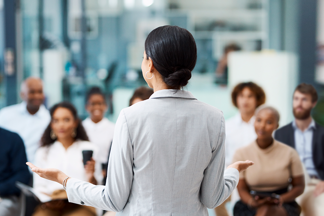 Mulher, em frente a um grupo de executivos, durante uma apresentação profissional