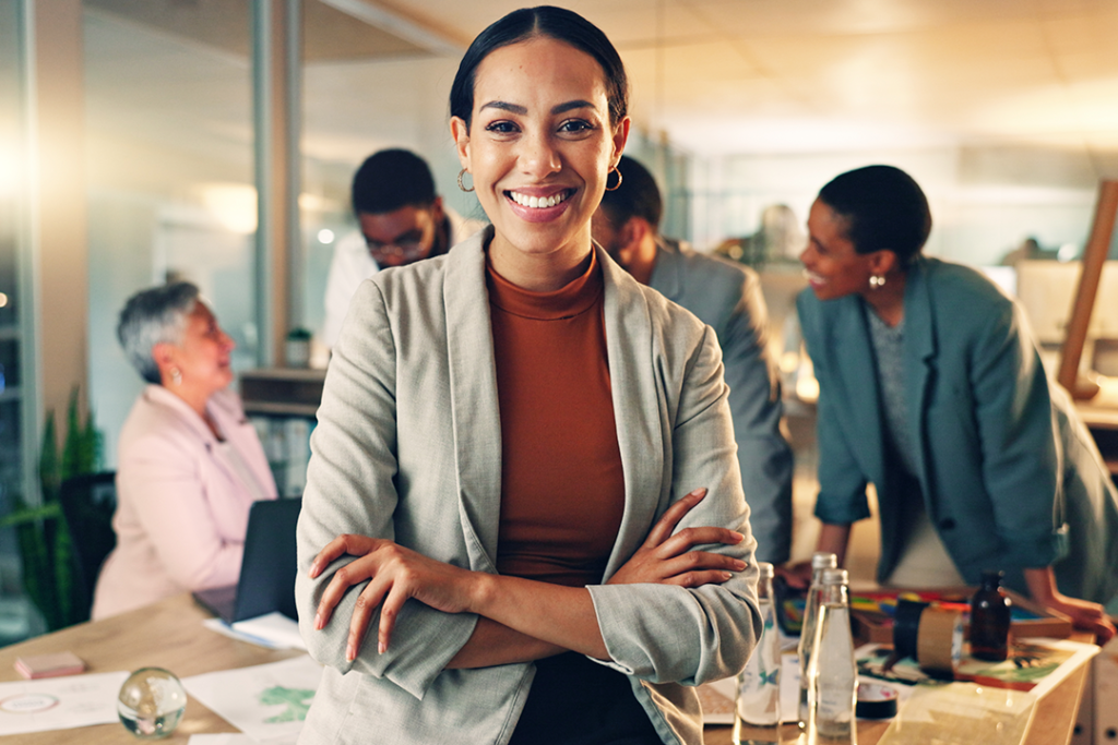 Mulher líder sorridente em ambiente de escritório moderno, com colegas ao fundo.