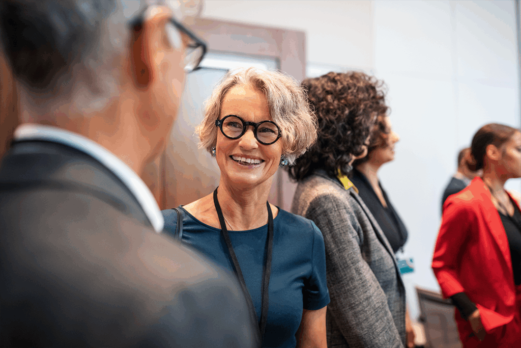 Foto de profissionais trocando sorrisos e conversando em um ambiente corporativo. Destaca a importância do networking humano como tendência para eventos atuais
