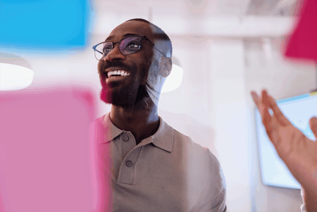Homem negro sorri e olha para post its durante dinâmica para construir pensamento criativo