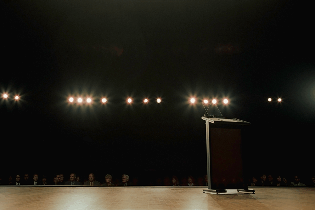 Foto de um palco iluminado com púlpito vazio e plateia à espera; o cenário ideal para a manifestação de emoções em cima do palco em uma apresentação impactante
